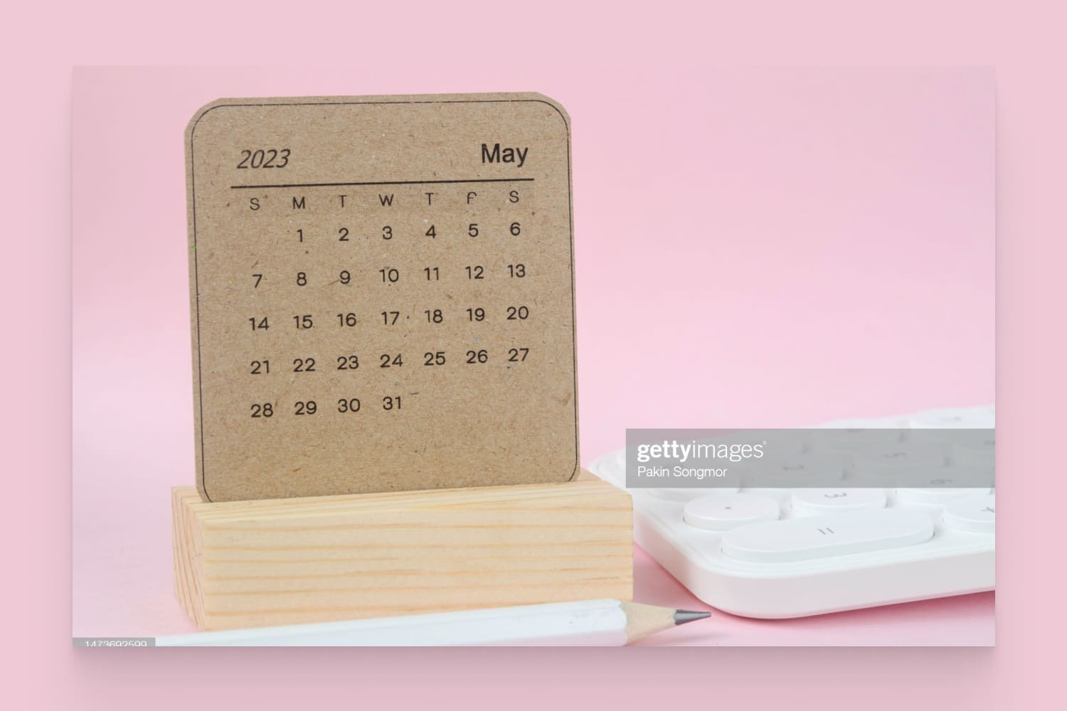 Calendar for May 2023 with a white pencil and calculator against a pink paper background