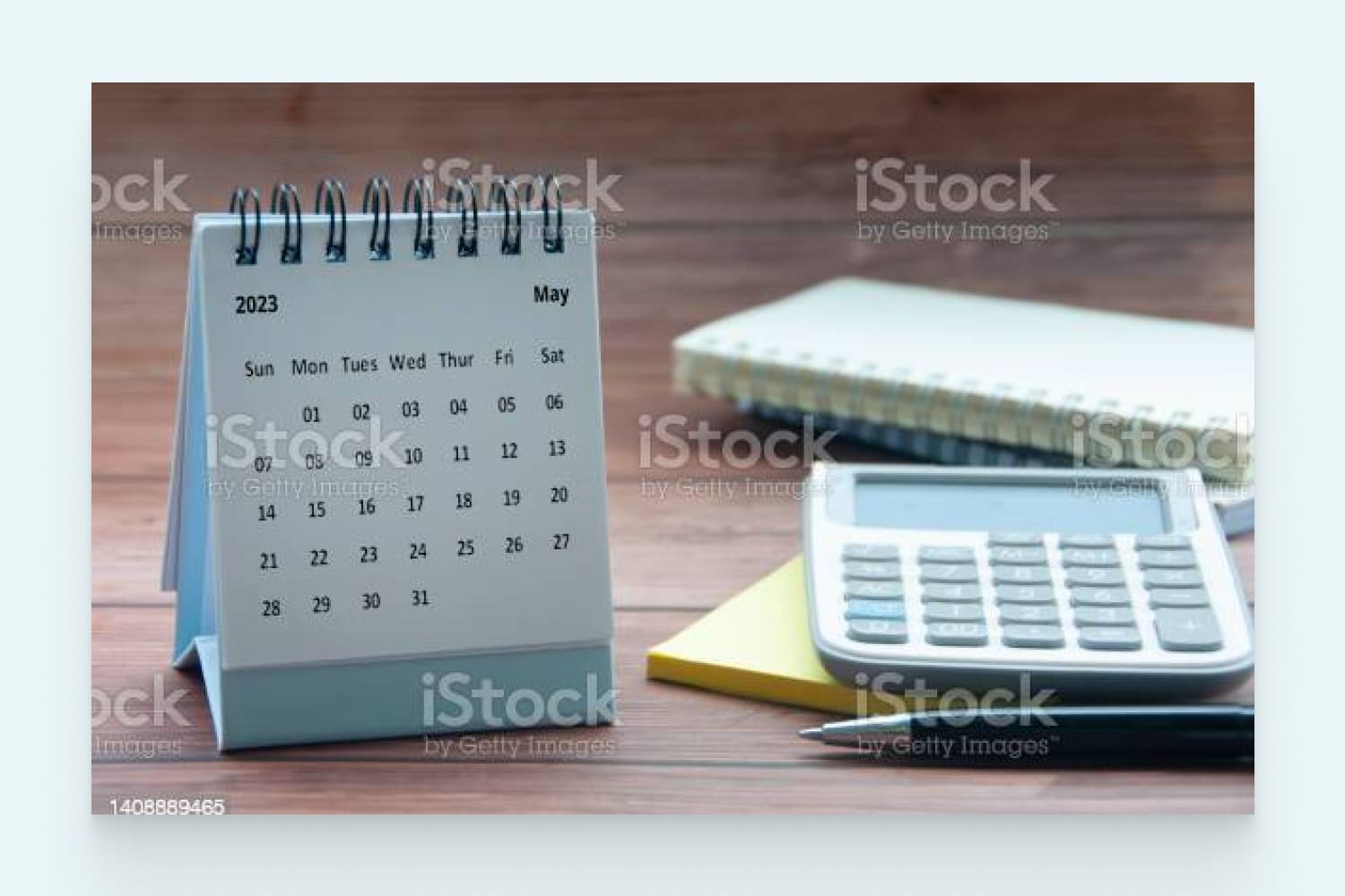 May 2023 white desk calendar on wooden table with notepad, calculator and pen background