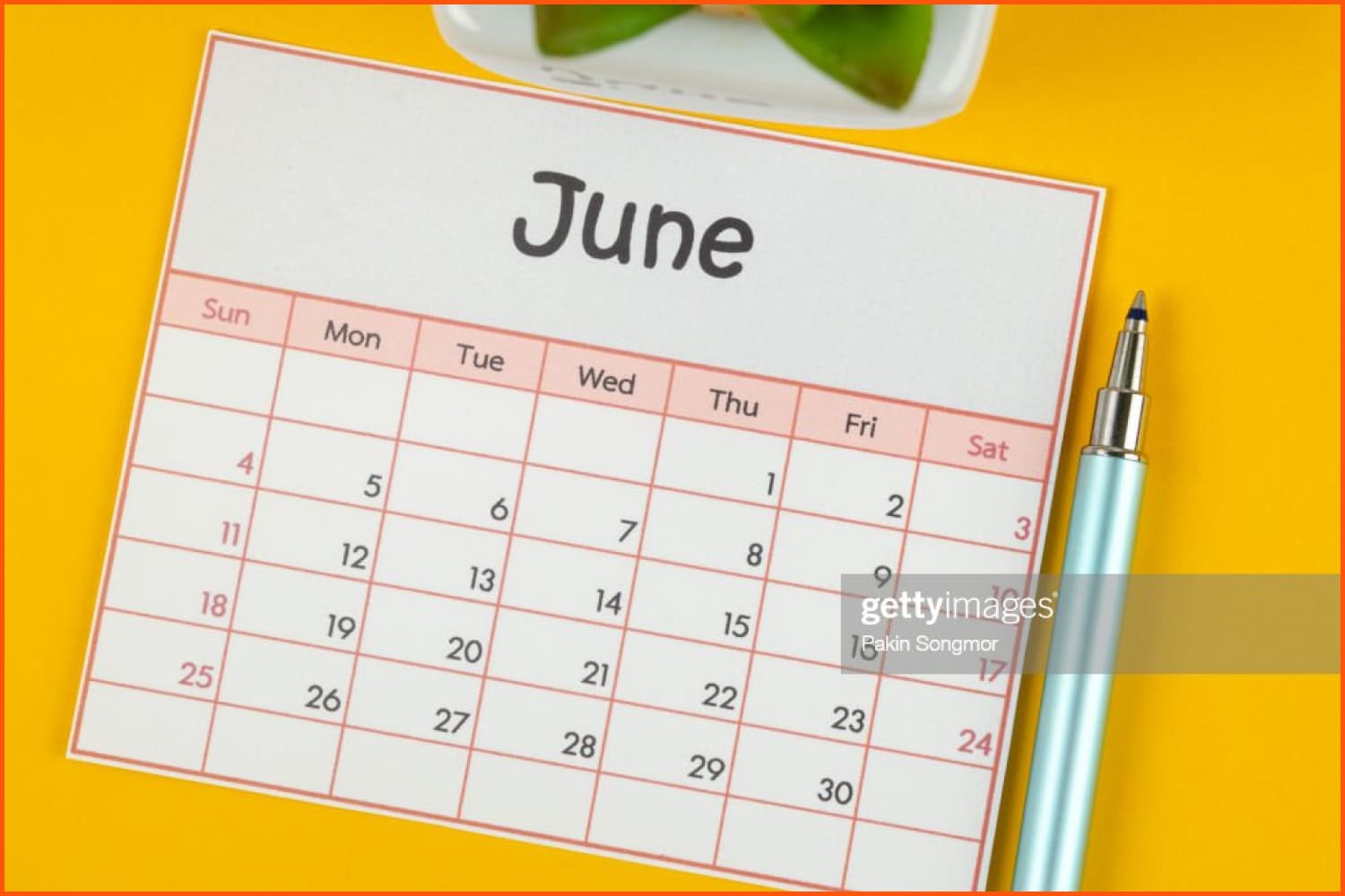 June calendar and a pen next to it on a yellow table.