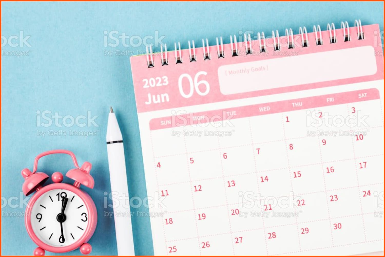June calendar, pen, pink alarm clock on blue table.