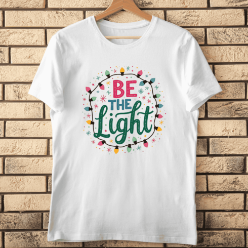 Be The Light Hand Lettering with String Lights T-Shirt Design cover image.