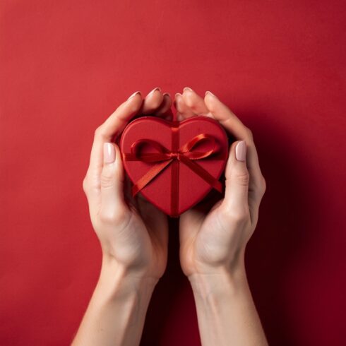 Female Hands Holding Heart Shaped Gift Box on Red Background Valentine Celebration cover image.