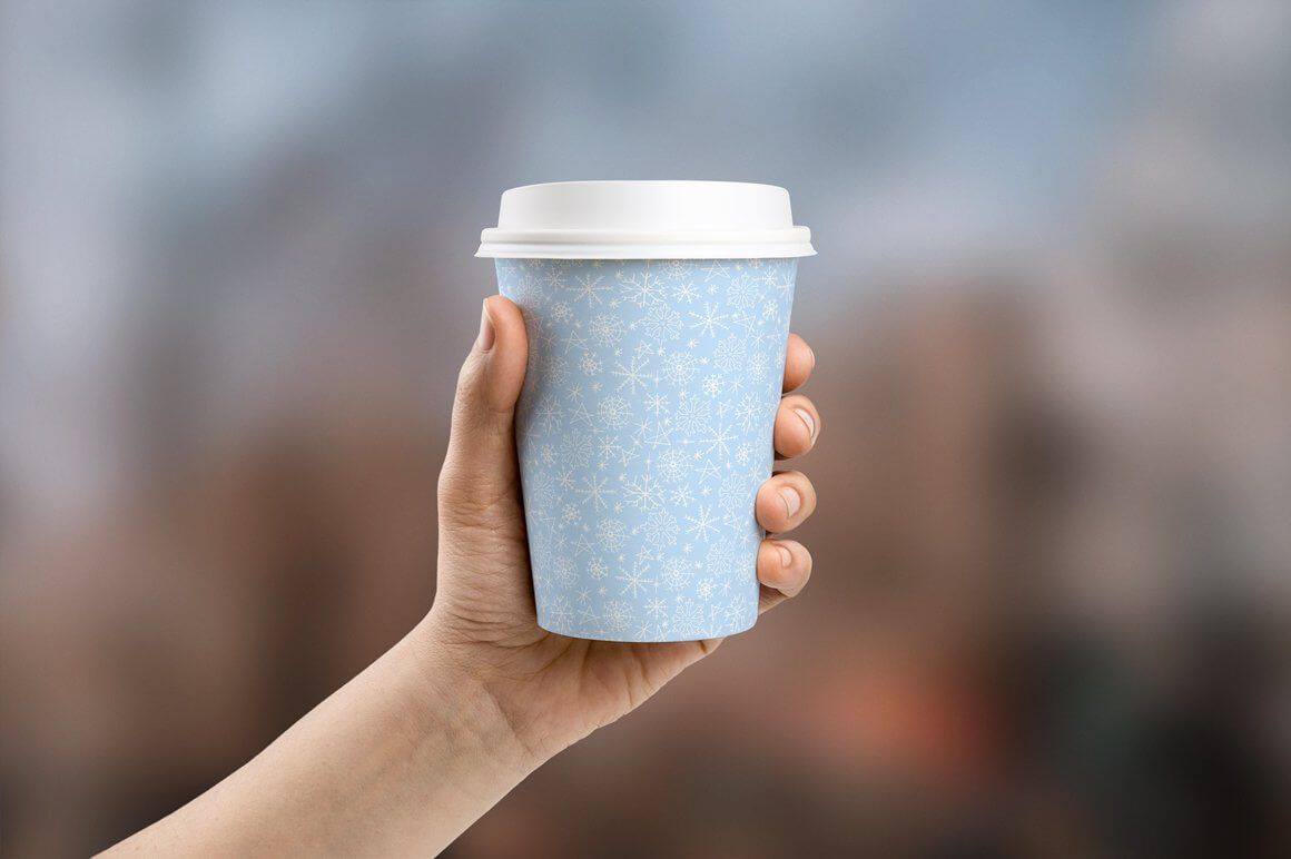 In his hand is a blue cup of coffee with a winter design and a white lid.