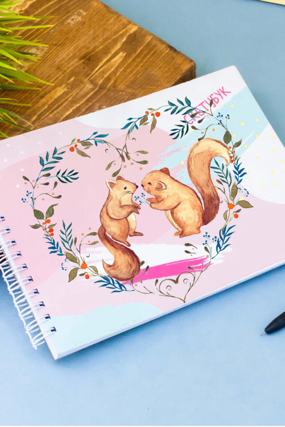 On the children's album, two squirrels are drawn that look at each other, and a heart is drawn around them with plants.