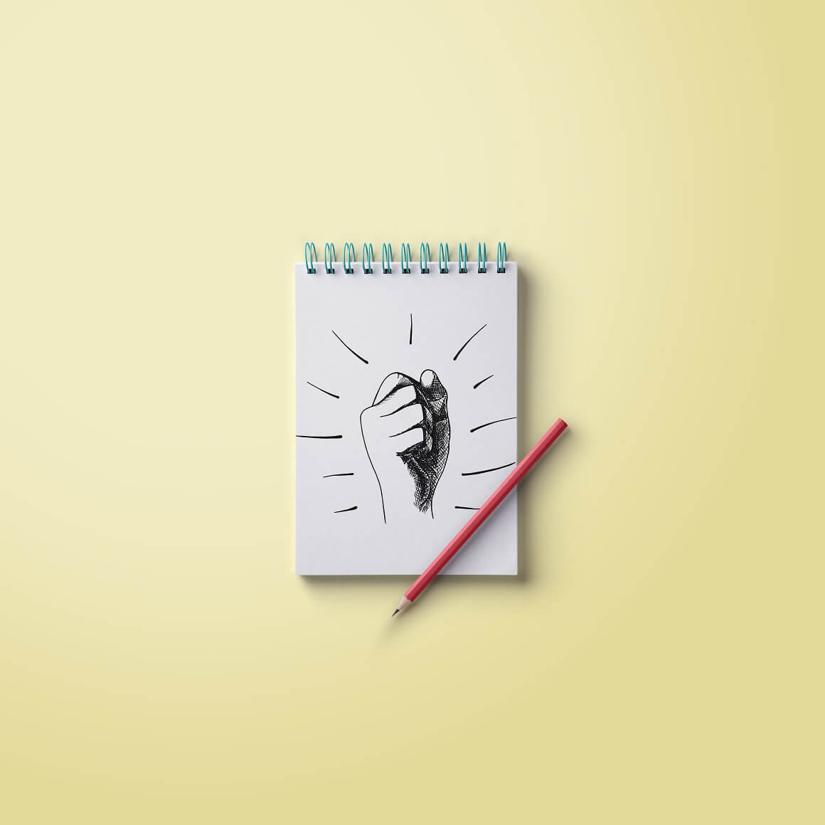 Drawing a fist with a red pencil on a white sheet of notebook lying on a yellow table.