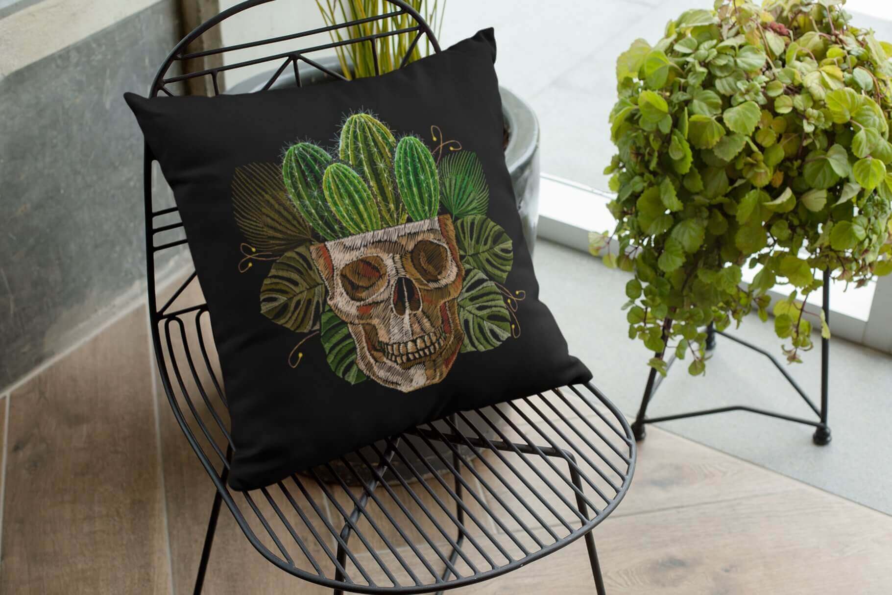 An embroidered skull from which cacti grow on a black pillow.