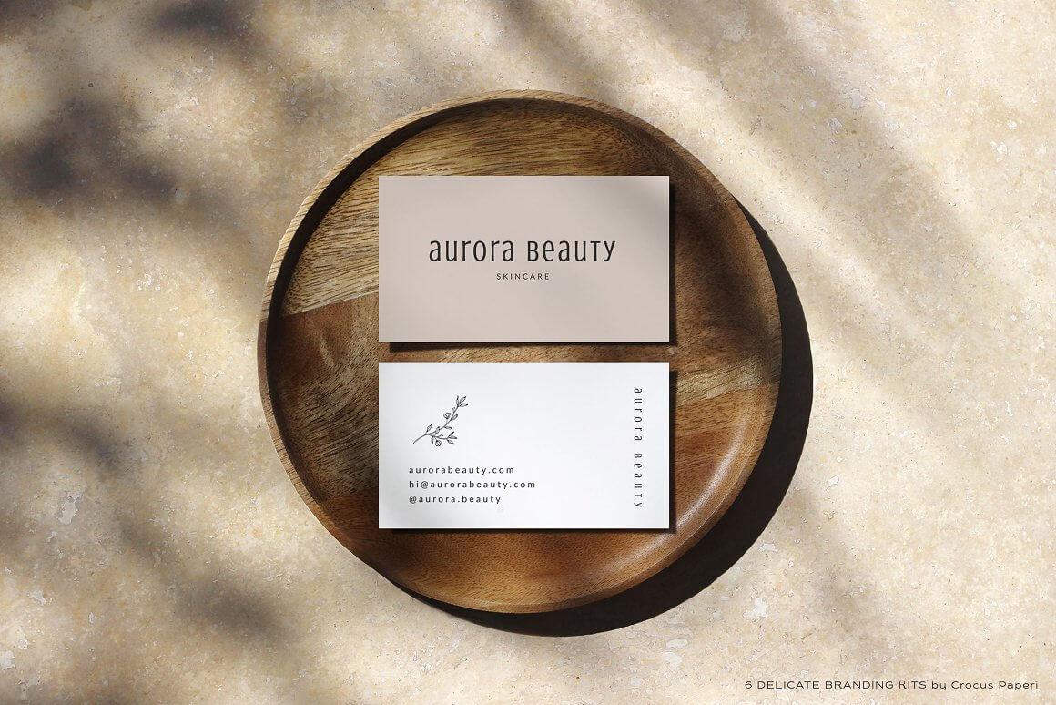 There are two identical business cards on a wooden plate, on one side of the business card is written aurora beauty, and on the other side all contacts are written.