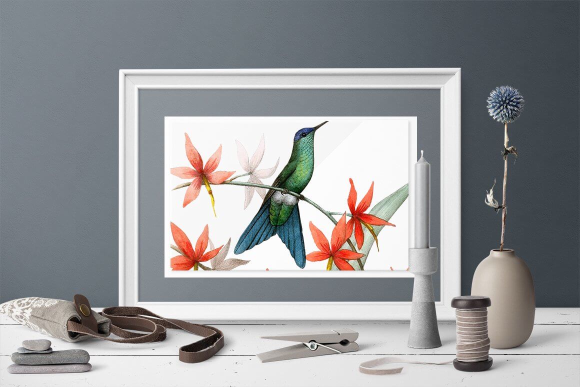 An image of a green hummingbird with a blue tail on a branch with red flowers in a painting that is in a gray room.