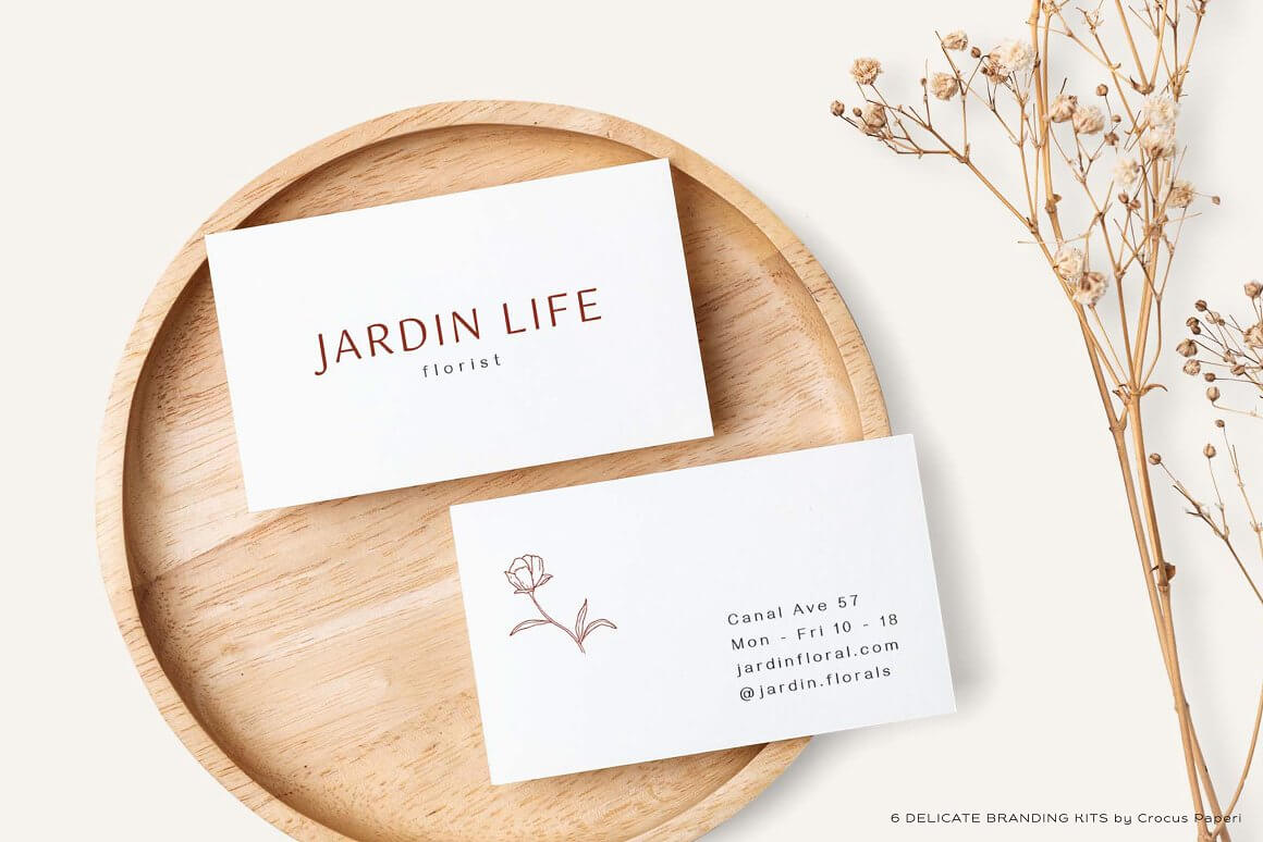 Business card Jardin life florist lies on a beige wooden product and next to it is a beautiful small twig.