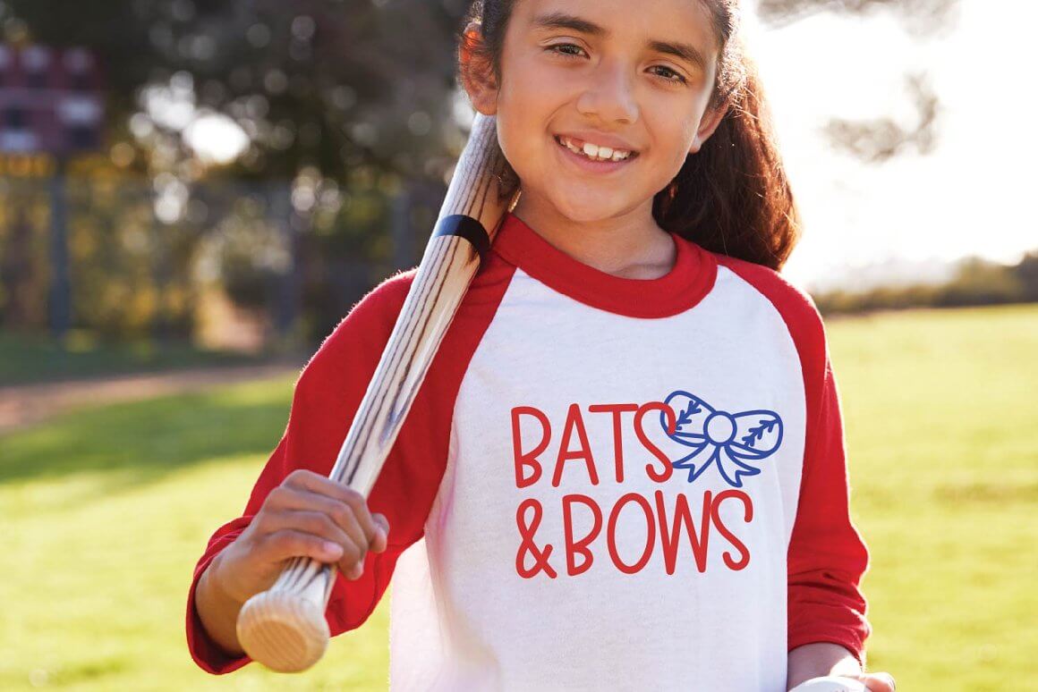 A girl in a baseball uniform with a bat on the background of a green lawn.