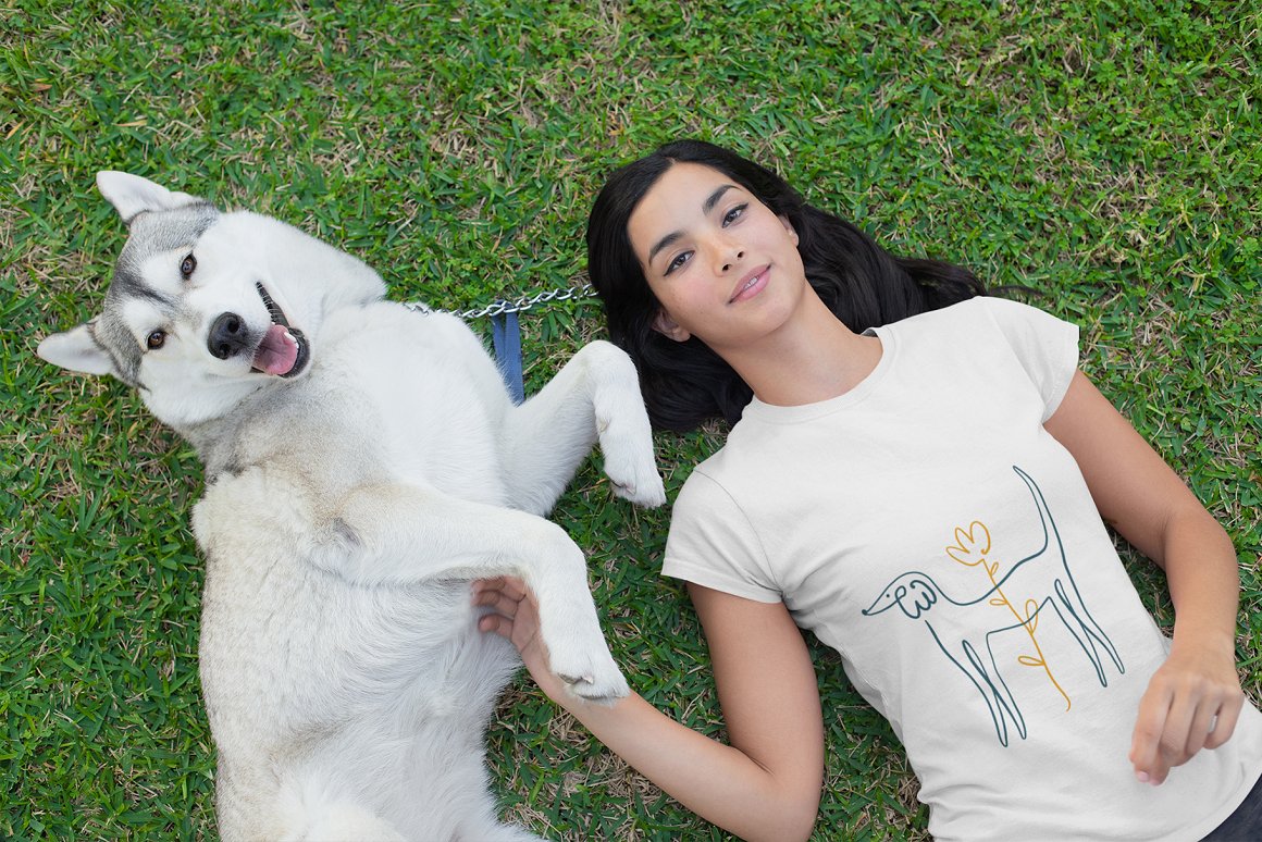 A girl with a husky dog lies on the grass.