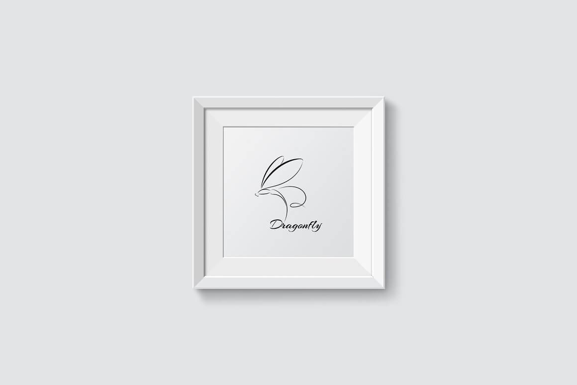 Black dragonfly logo on a white picture in a white frame on a white wall.