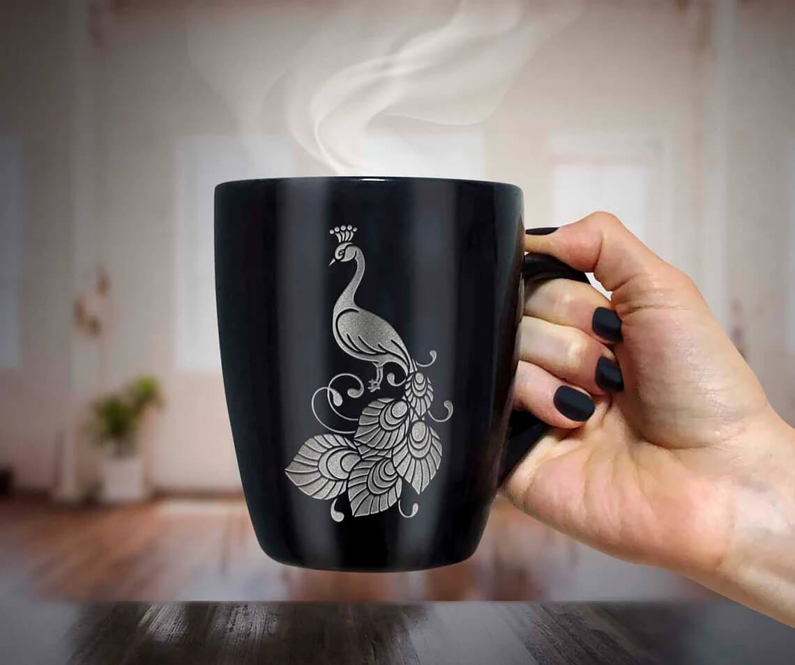 Woman holding a black coffee cup with a white peacock on it.