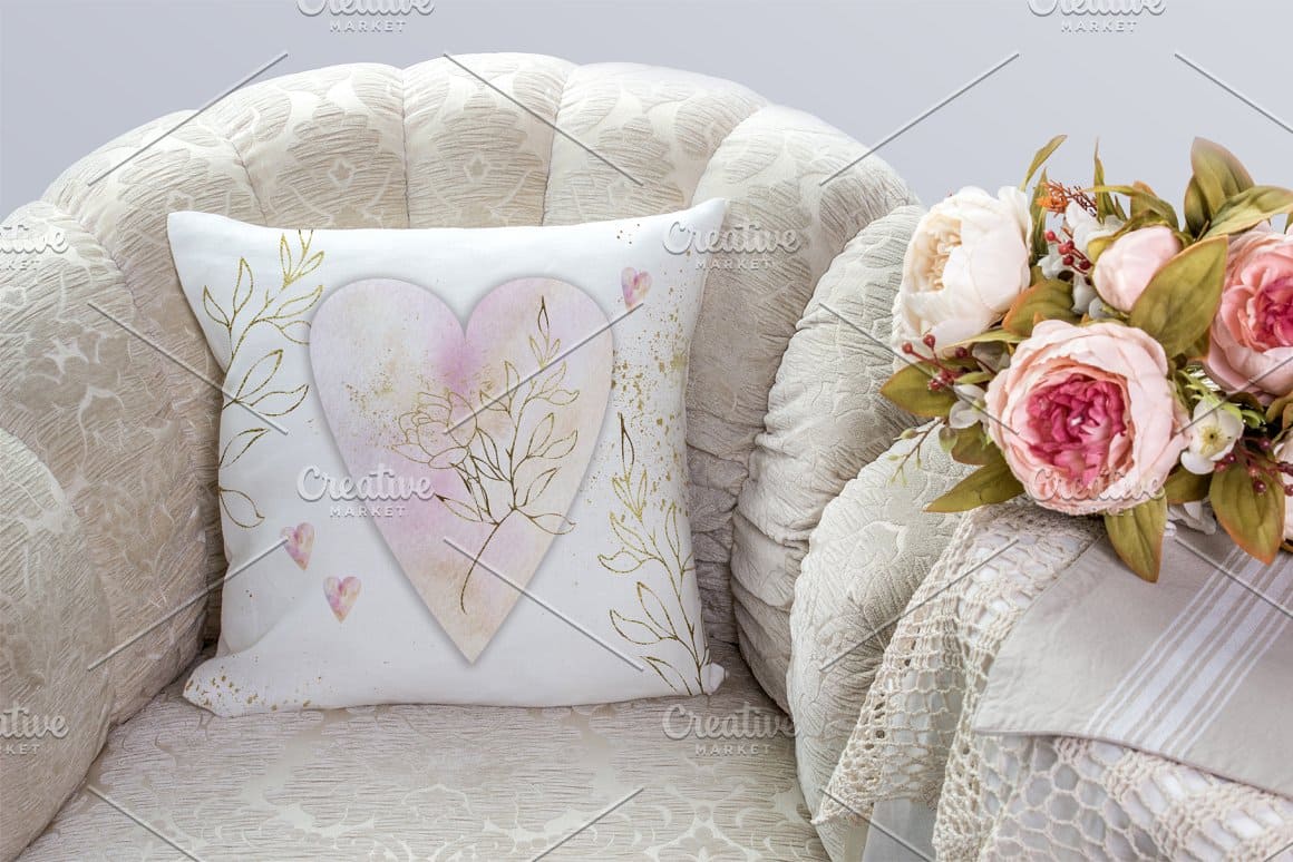 A white pillow with a golden outline of flowers and a watercolor painted heart.