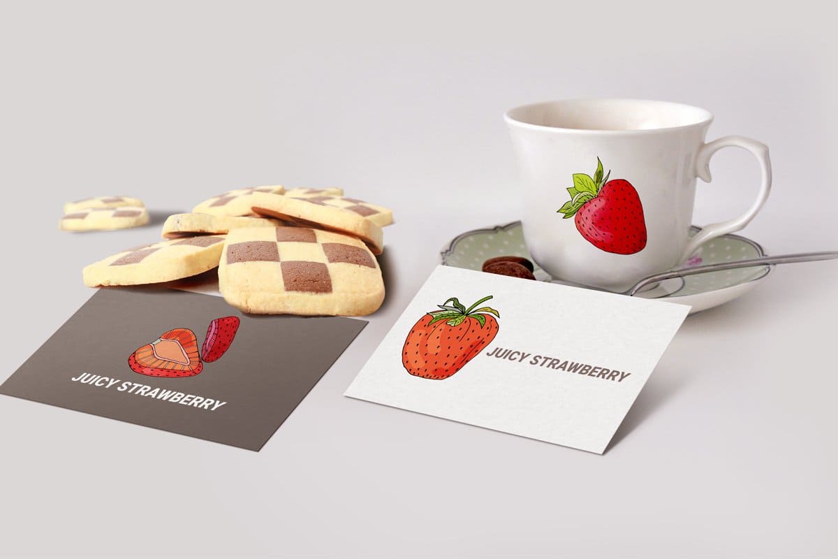 A white cup with a picture of strawberries and a shortbread cookie next to the cup.