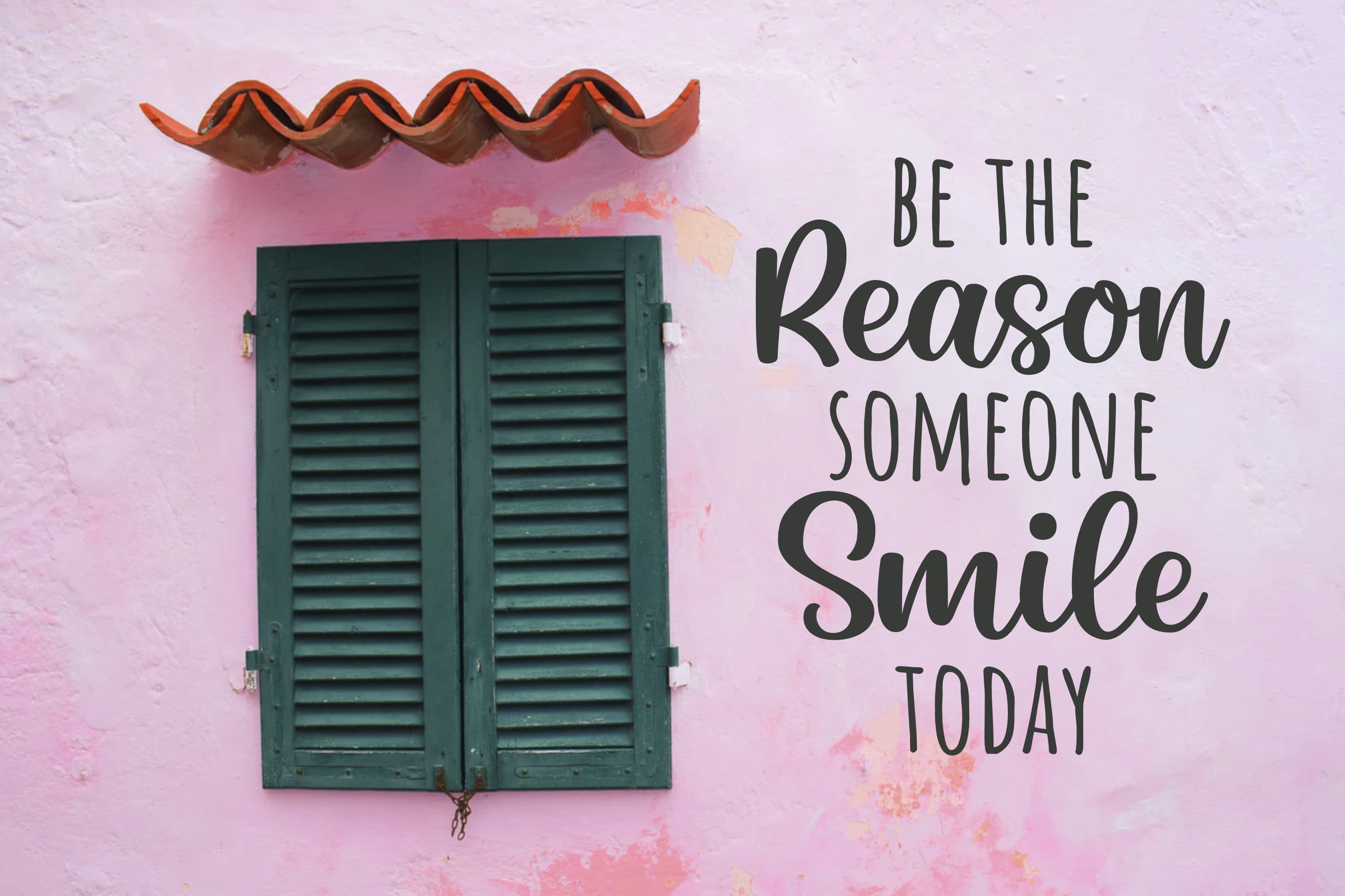 Green shutters on the background of a pink wall and the inscription "Be the Reason Someone Smile Today".