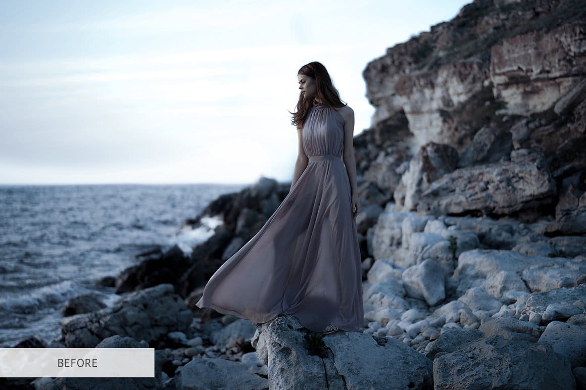 A dark photo of a girl standing in a dress by the sea.